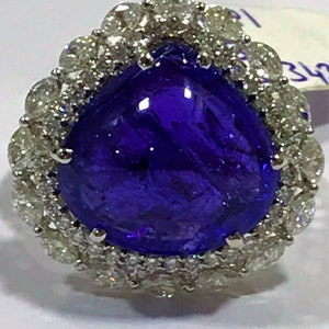May include: A pear-shaped, deep blue gemstone ring surrounded by a halo of smaller, white diamonds.