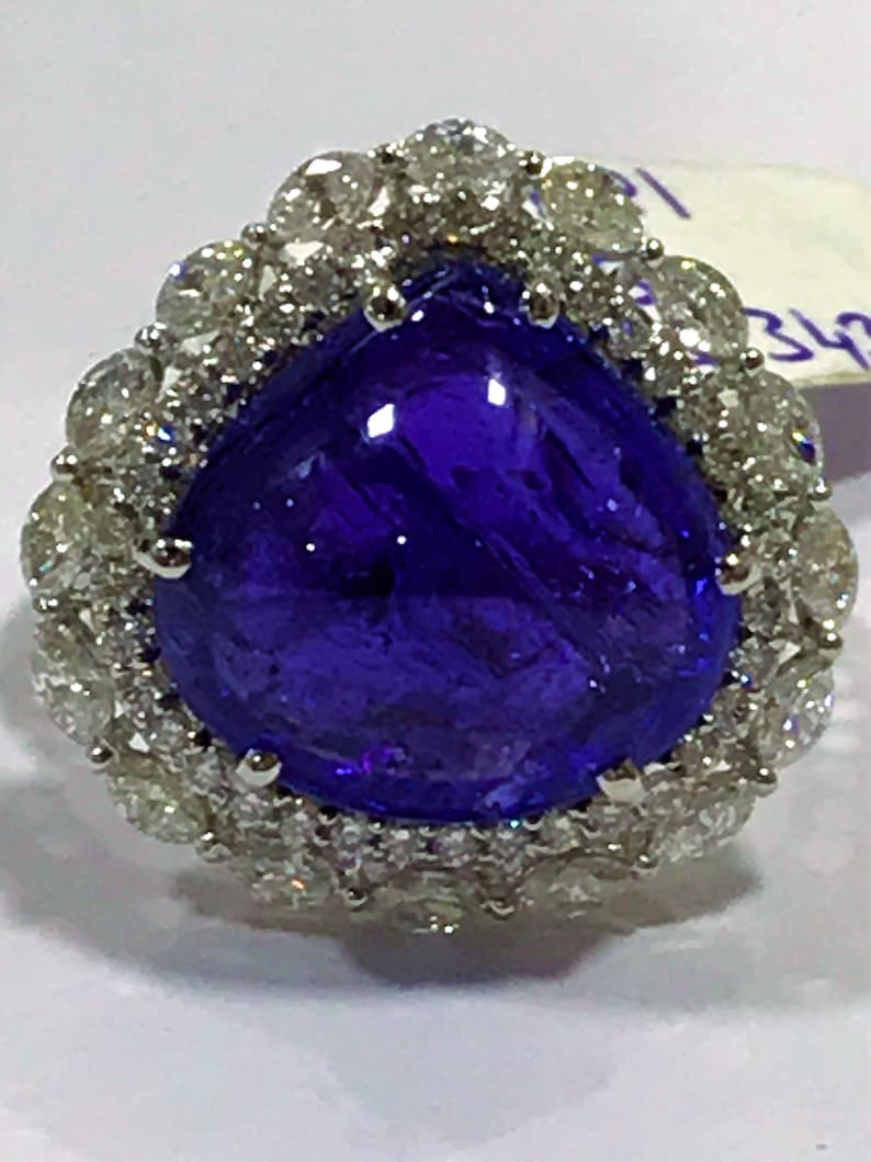 May include: A pear-shaped, deep blue gemstone ring surrounded by a halo of smaller, white diamonds.