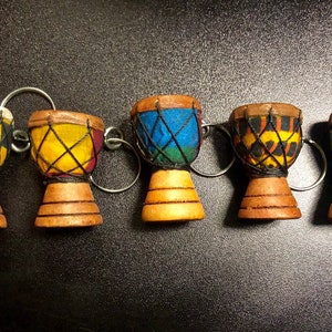May include: Six miniature wooden djembe drums with colorful patterned fabric heads. Each drum has a metal ring attached and is a keychain.