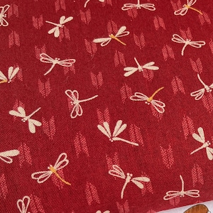 May include: Two fabric swatches with a dragonfly pattern. The top swatch is red with white dragonflies. The bottom swatch is navy blue with white dragonflies. The swatches are folded over each other and a white tag with Japanese text is visible.
