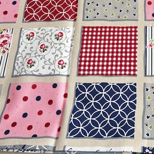 Könnte beinhalten: Ein Stoff mit einem Raster aus Quadraten mit verschiedenen Mustern, darunter rotes Vichy-Karo, rosa Punkte, marineblaue Kreise und florale Motive. Ein 76 cm langes Holzlineal liegt horizontal oben auf, dazu ein rundes weißes Etikett.