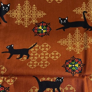 Puede incluir: Tela naranja con un patrón repetido de gatos negros, diseños ornamentados dorados y motivos florales coloridos. La tela tiene una etiqueta que dice "#12 -  Koushimatsu"