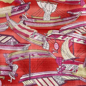 May include: Red fabric with a repeating pattern of pink and white boats. The fabric has a subtle sheen and a textured surface.