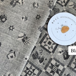 Könnte beinhalten: Zwei Stoffmuster mit einem schwarz-weißen geometrischen Muster. Der Stoff links ist hellgrau mit einem kleineren Muster. Der Stoff rechts ist dunkelgrau mit einem größeren Muster. Der Stoff rechts hat ein weißes Etikett mit dem Text "MOZHENHANDMADE" in Schwarz.