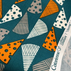 Op de afbeelding: Teal stof met een herhalend patroon van oranje, witte en grijze geometrische vormen. De stof heeft een wit label met de tekst "Cotonienne "setort" "cheche" | designed by anyan"