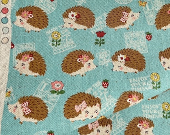 May include: A teal fabric featuring a repeating pattern of cartoon hedgehogs, flowers, and strawberries. The hedgehogs have brown quills and wear floral accessories. The fabric has a raw edge and a tag with Chinese text.