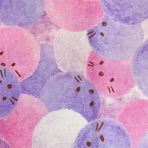 以下が含まれることがあります： 水彩の円の中に漫画の猫の顔が描かれた、ピンクと紫の生地。円は様々なサイズで重なり合っている。