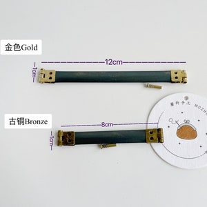 Könnte beinhalten: Zwei Metallschließen für einen Taschenriemen, eine in Gold und eine in Bronze. Die Schließen sind 1 cm breit und die Riemen sind 12 cm und 8 cm lang. Die Schließen werden auf einem weißen Hintergrund gezeigt.