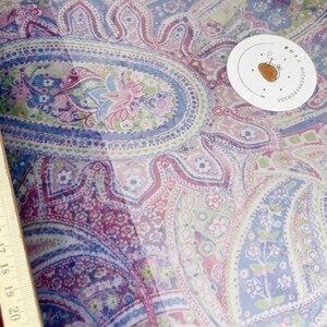 Peut inclure: Un tissu transparent avec un motif paisley dans des tons de rose, violet, bleu et vert. Le tissu a un fond blanc et est décoré d'un motif paisley répété.