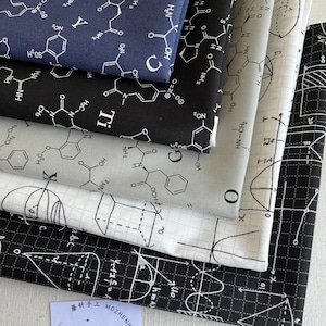 May include: A stack of four fabric squares with different science-themed patterns. The top square is a dark blue fabric with white chemical formulas. The second square is black fabric with white chemical formulas. The third square is white fabric with black chemical formulas. The bottom square is black fabric with white geometric shapes and a grid pattern. The fabric squares are labeled with the text "蘑针手工 MOZHENHANDMADE".