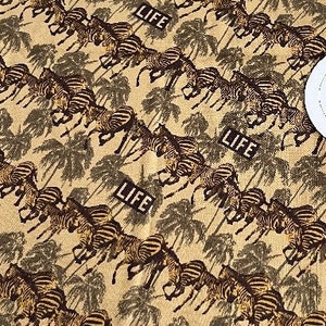 May include: A beige fabric with a repeating pattern of black and white zebras running through a jungle scene. The word "LIFE" is repeated throughout the fabric.