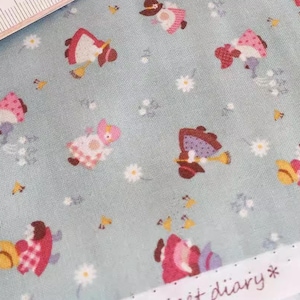 Puede incluir: Primer plano de muestras de tela con un patrón repetido de personajes de dibujos animados con sombreros y vestidos, con pequeñas flores blancas y detalles amarillos. Una regla está colocada sobre la tela. El texto "Sweet diary" es visible.