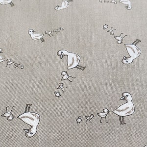May include: A beige fabric with a repeating pattern of white birds and their chicks. The birds are facing different directions and some are holding their wings out. The fabric has a subtle texture.