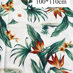 May include: White fabric with a tropical print featuring green leaves, orange and yellow flowers, and a white label with the text "100*110cm".