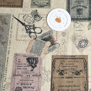 Può includere: Un tessuto beige con un motivo ripetitivo di etichette e illustrazioni in stile vintage. Le etichette presentano testi come "Blue Castle", "Sewing Machine", "Floral Pattern" e "Royal". Le illustrazioni includono forbici, rocchetti di filo e altri oggetti legati alla cucitura.