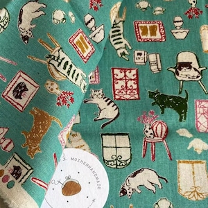 May include: Teal fabric with a repeating pattern of cats, houses, and other objects. The fabric is made in Japan and has a label that says "Mozhenhandmade".