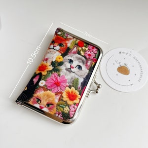 May include: Embroidered coin purse with a floral design and several cats. The purse is approximately 10.5cm tall and 7cm wide, with a silver metal clasp. A tag with a drawing of a purse is next to the purse.