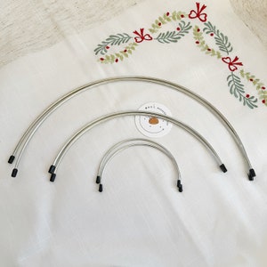 May include: Four silver hoops with black plastic ends, arranged in a graduated size order, on a white fabric background.