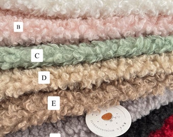 May include: A stack of six different colored faux fur fabrics. The fabrics are arranged from top to bottom in the following order: white, pink, green, beige, gray, and black. The bottom layer is red. The fabrics are all soft and fluffy.