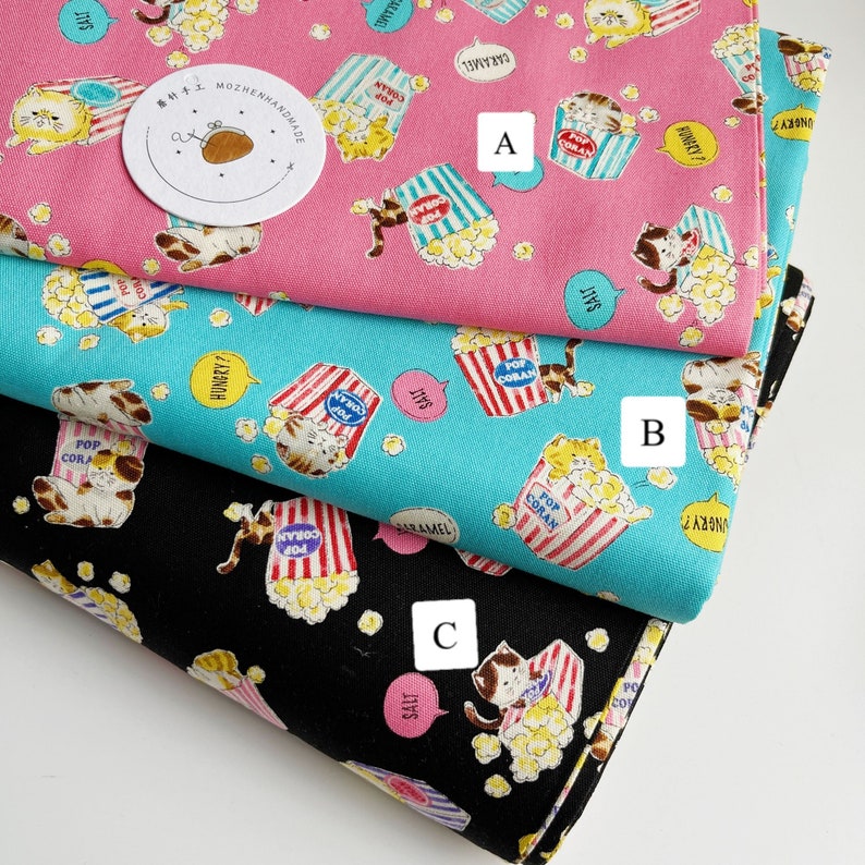 May include: Three fabric swatches with a repeating pattern of cats eating popcorn. The top swatch is pink, the middle swatch is turquoise, and the bottom swatch is black. Each swatch has a different text bubble with a different flavor of popcorn: salt, caramel, and hungry?.