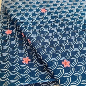 Op de afbeelding: Blauwe stof met een wit golvend patroon en roze bloemaccenten. De stof is dubbelgevouwen.