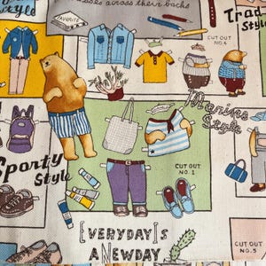 Op de afbeelding: Een kleurrijke stof met papieren poppen uitknippen in verschillende stijlen, waaronder sportief, maritiem, traditioneel en alledaags. De stof heeft illustraties van dieren, kleding en accessoires. De tekst "Everyday is a new day" is op de stof gedrukt.