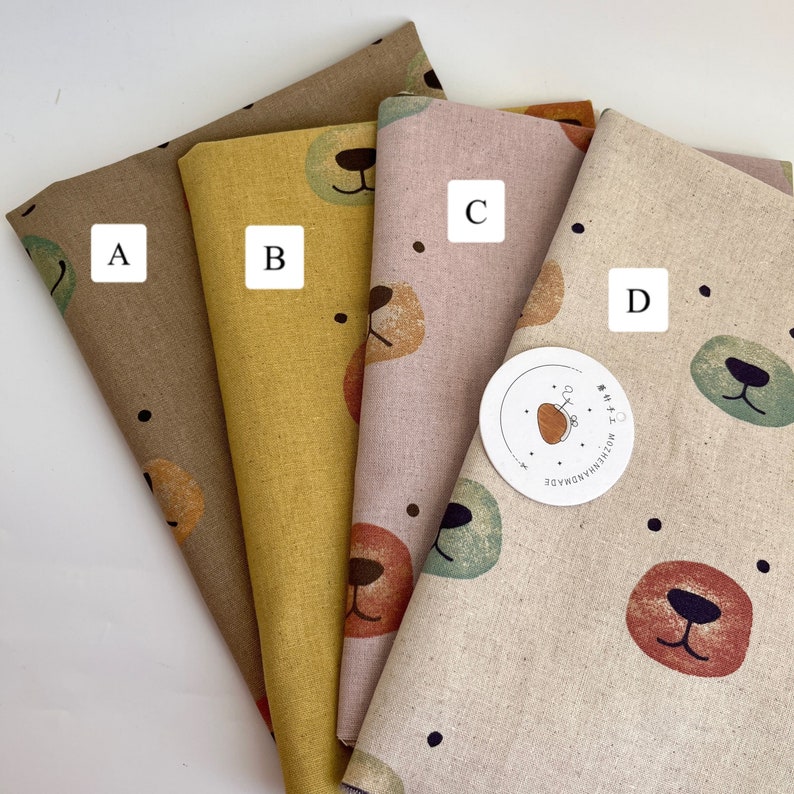 May include: Four fabric swatches with different patterns of brown, yellow, pink, and beige with a bear face design. The swatches are labeled A, B, C, and D.