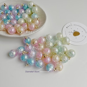 Könnte beinhalten: Eine Sammlung von irisierenden Glasperlen mit goldenen Akzenten. Die Perlen haben einen Durchmesser von etwa 1,6 cm und sind in verschiedenen Pastellfarben erhältlich, darunter Rosa, Blau und Gelb.