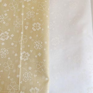 May include: Two fabric swatches, one beige with a white four-leaf clover pattern and one white with a faint white four-leaf clover pattern.