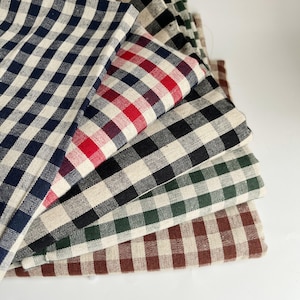 May include: A selection of folded fabric pieces in a range of colours, including navy, red, black, green, and brown. Each fabric features a classic white and coloured check pattern. The fabrics are stacked on a white surface.