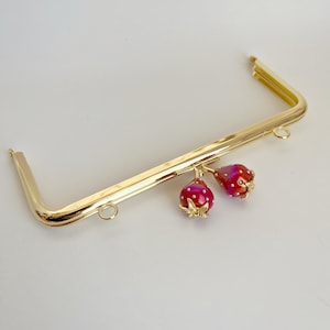 May include: Gold metal purse frame with two red and white strawberry charms.