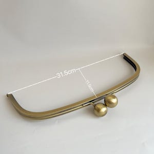 Op de afbeelding: Gouden metalen handtaschenframe met twee ronde sluitingen. Het frame meet 29,2 cm bij 80 cm.