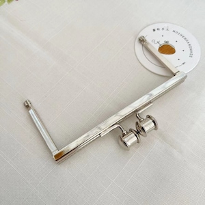 May include: Silver-toned metal purse frame with two round clasps. The frame is open and ready to be attached to a purse.