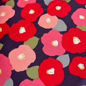 以下が含まれることがあります： 濃い青色の生地に、ピンクと赤の椿の花が繰り返し模様になっている。花の中心は白く、緑の葉で囲まれている。