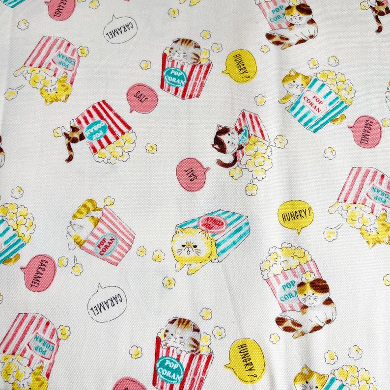 May include: White fabric with a repeating pattern of cats holding boxes of popcorn. The boxes are red and white striped with blue and white stripes. The text on the boxes reads "Pop Corn" and "Caramel". The cats are wearing different expressions and some have speech bubbles with the words "Hungry?" and "Salt".