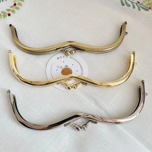May include: Three metal purse frames in different finishes: antique brass, gold, and silver. The frames are curved and have a decorative design at the top.
