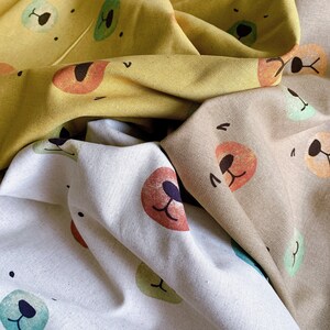 May include: Three fabric swatches with different colored backgrounds and bear face patterns. The first swatch is yellow with a brown bear face, the second is beige with a red bear face, and the third is white with a green bear face.