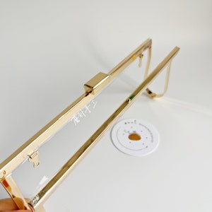 May include: Gold metal frame with a clear plastic insert. The frame is open and the clasp is visible. The frame is designed for a clutch purse.