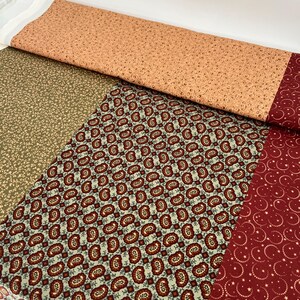 May include: A fabric with four different patterns. The top pattern is a light orange with a small brown floral design. The second pattern is a dark green with a small brown floral design. The third pattern is a light green with a small red and brown paisley design. The bottom pattern is a dark red with a small white star design.