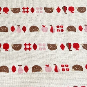 May include: A white fabric with a repeating pattern of brown hedgehogs, red apples, pink pears, red leaves, and red and white checkered squares.