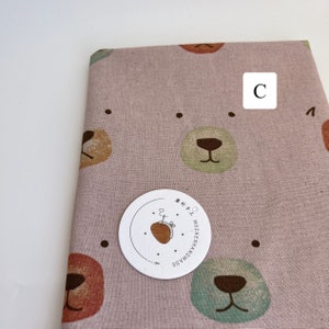 May include: Pink fabric with a repeating pattern of brown bear faces. The fabric has a subtle texture and is perfect for crafting projects. The fabric is labeled "HANDMADE NOZZHENH" in Japanese.