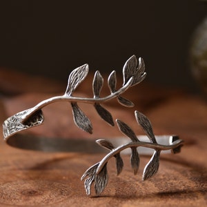 May include: Silver bracelet with a delicate leaf design. The bracelet is open and has a textured band.