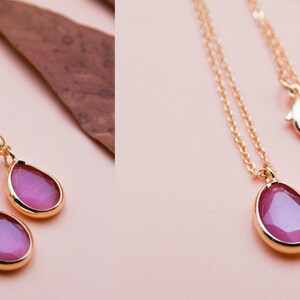 May include: A gold necklace and earrings set with pink teardrop-shaped stones. The necklace has a delicate chain and a lobster clasp closure.