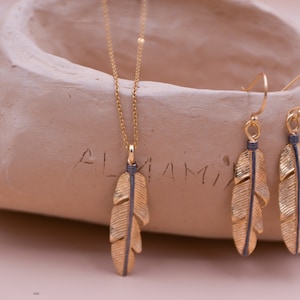 May include: A gold necklace and earrings set featuring a feather pendant and matching earrings. The feather is gold with a black stripe down the center.