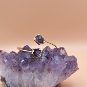 Puede incluir: Un brazalete de oro con dos piedras de amatista. El brazalete est&aacute; apoyado en un grupo de cristales de amatista.