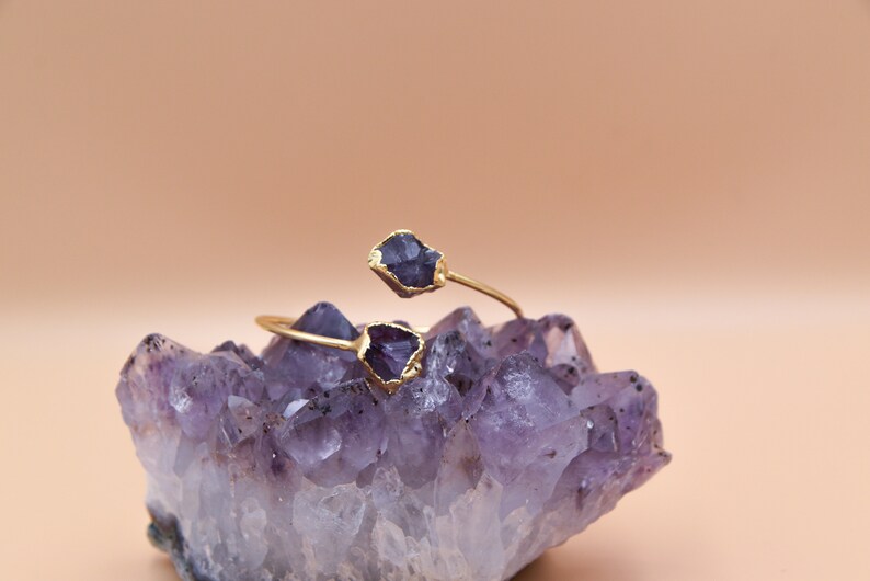 Puede incluir: Un brazalete de oro con dos piedras de amatista. El brazalete est&aacute; apoyado en un grupo de cristales de amatista.
