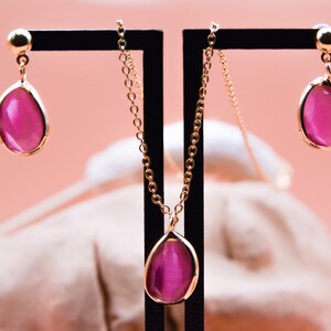 May include: A gold chain necklace and earrings with a teardrop-shaped pink stone pendant and matching earrings.
