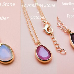 May include: Three gold necklaces with teardrop-shaped pendants. The pendants are made of tanzanite, tourmaline, and amethyst stones. The tanzanite stone is light blue, the tourmaline stone is pink, and the amethyst stone is purple. The necklaces are labeled with the stone name and the corresponding birth month: Tanzanite Stone & December, Tourmaline Stone & October, Amethyst Stone & February.