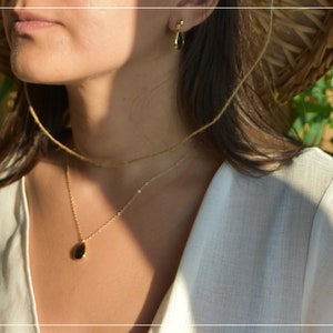 May include: A woman wearing a white shirt and a straw hat with a gold chain necklace with a small oval pendant.