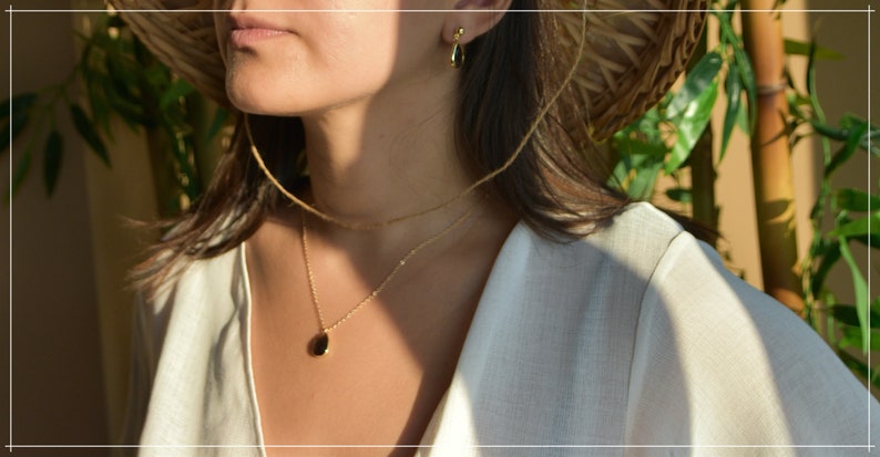 May include: A woman wearing a white shirt and a straw hat with a gold chain necklace with a small oval pendant.